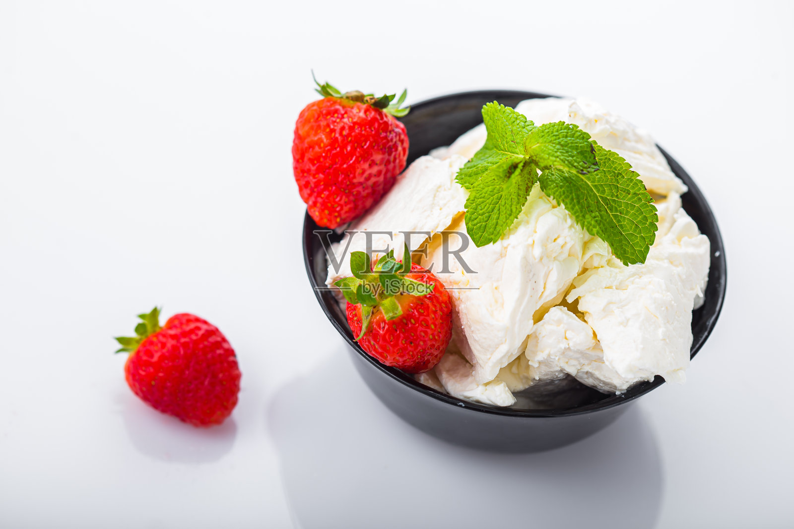 在一个黑色的盘子里，大块大块的白干酪、草莓和薄荷叶，在一个孤立的白色背景上照片摄影图片