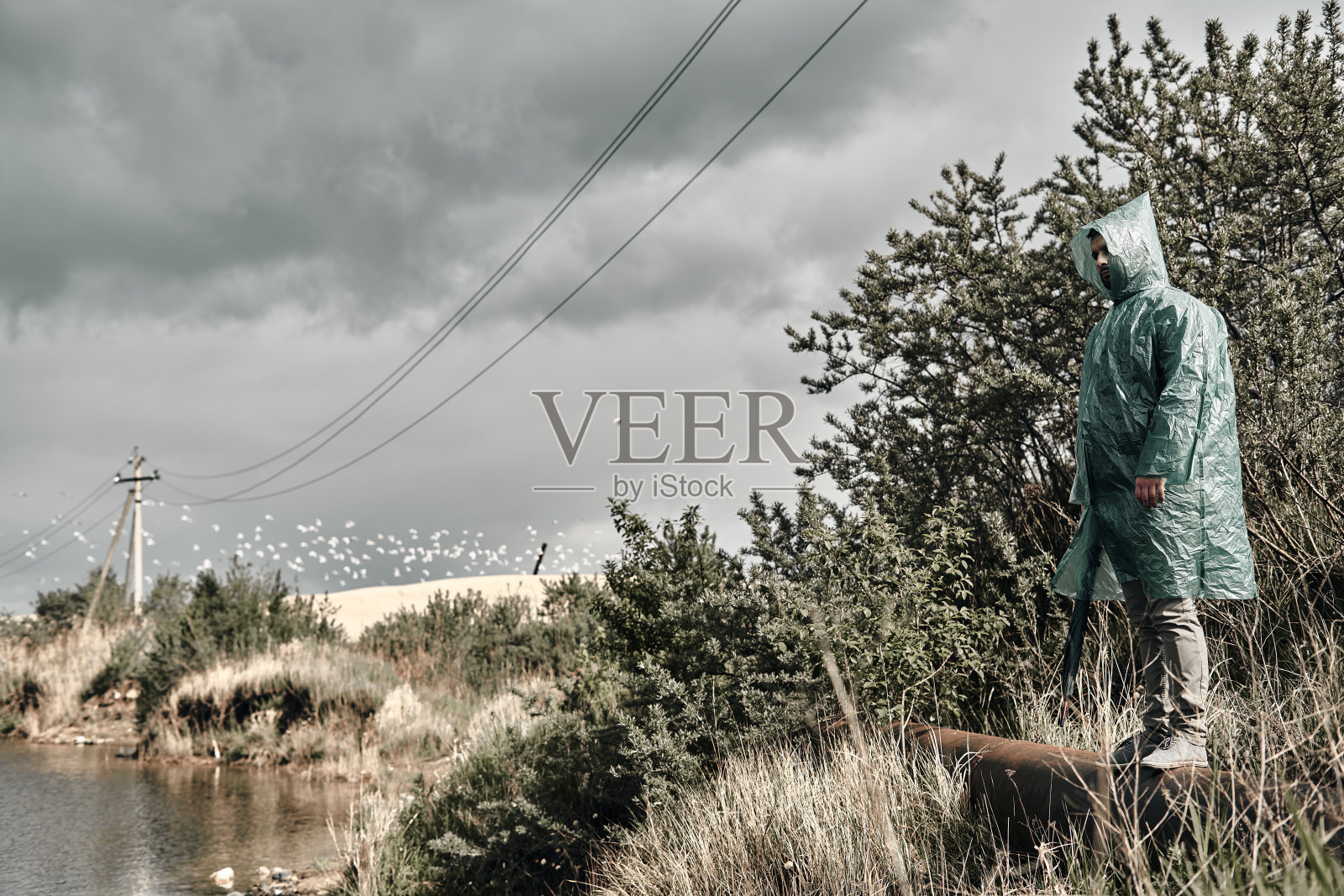 一个穿着绿色雨衣的人在岸边靠近水边。主要是多云的。照片摄影图片