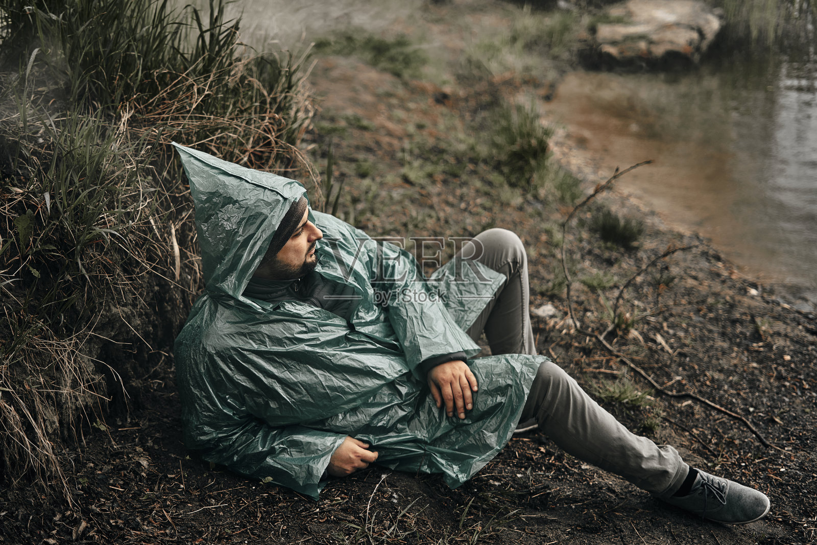 一个穿着绿色雨衣的人坐在大自然的地上。一个放松和休息的地方。照片摄影图片