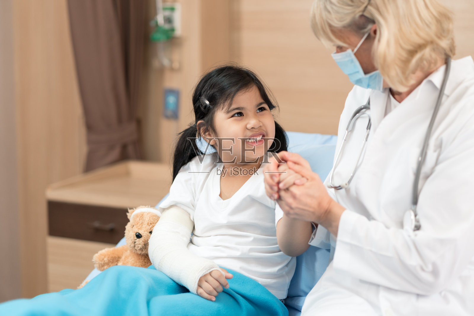 健康医疗中心年轻微笑的女儿科医生和带着泰迪熊的儿童患者，积极地与孩子交谈，给予鼓励照片摄影图片