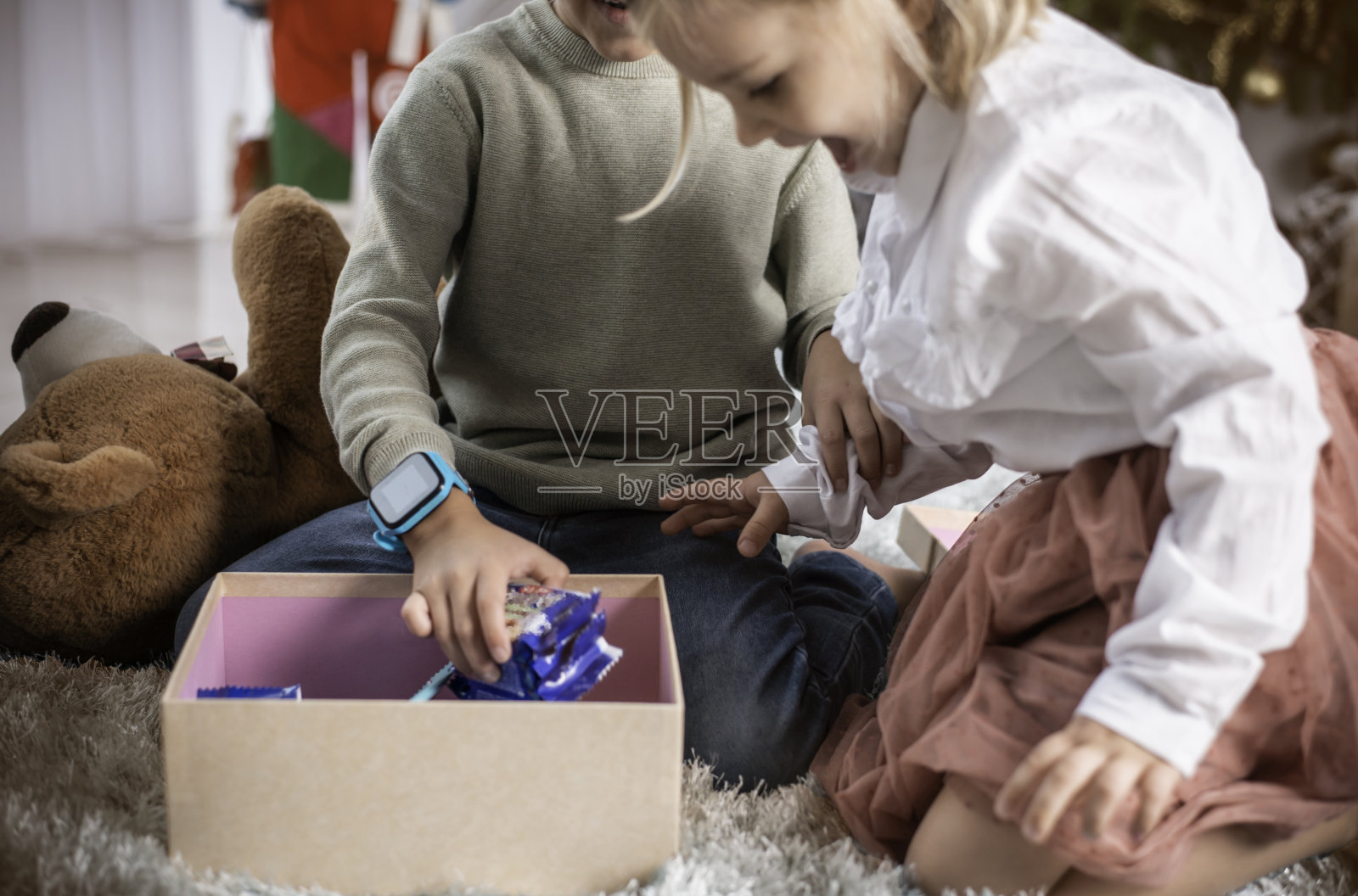 惊奇的小女孩在圣诞树旁打开礼物，打开礼物，孩子们在客厅里享受圣诞庆祝，欢乐的圣诞时光照片摄影图片
