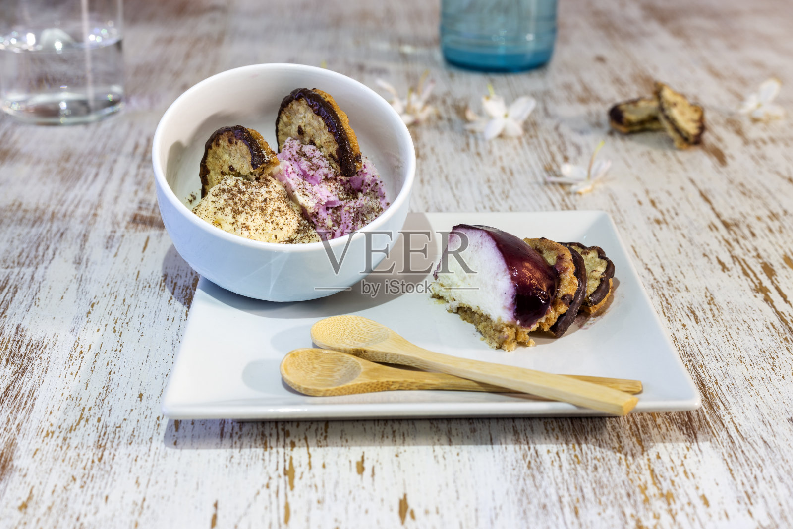 一块芝士蛋糕、蓝莓果酱、燕麦饼干和巧克力放在一个方形盘子里，放在一张风化的白色桌子上。碗里装两勺香草和草莓冰淇淋，还有燕麦饼干照片摄影图片