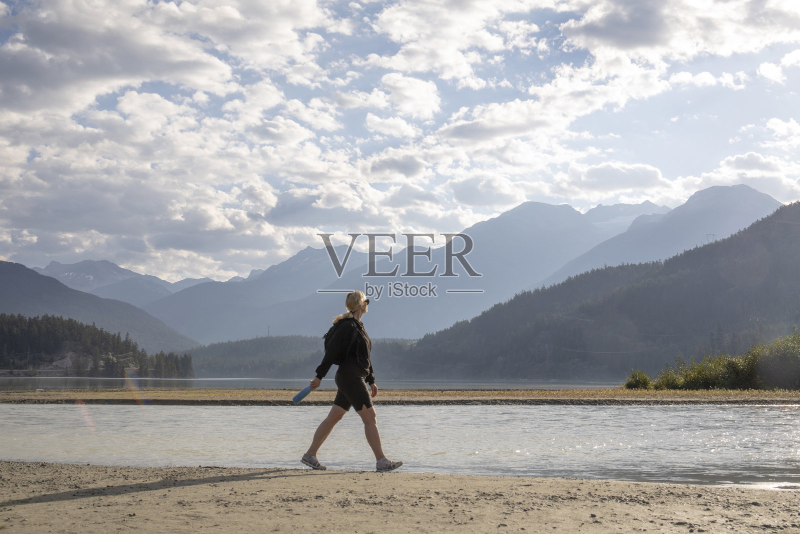 日出时，女人沿着湖岸散步照片摄影图片