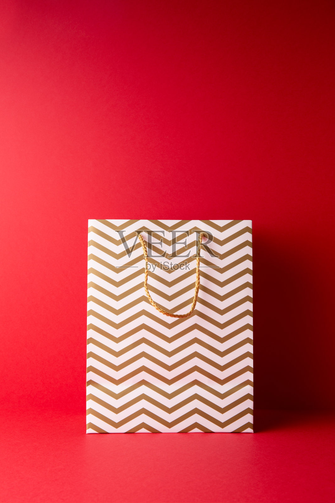白色纸袋与金色条纹在红色的背景。副本的空间。照片摄影图片