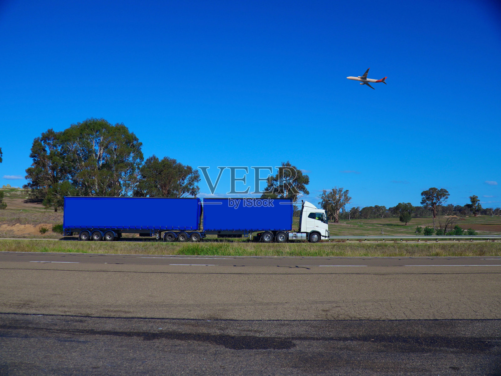 高速公路上的卡车和从头顶飞过的飞机，在悉尼和墨尔本之间的澳大利亚乡村小镇，美丽的蓝天和郁郁葱葱的树木作为背景照片摄影图片