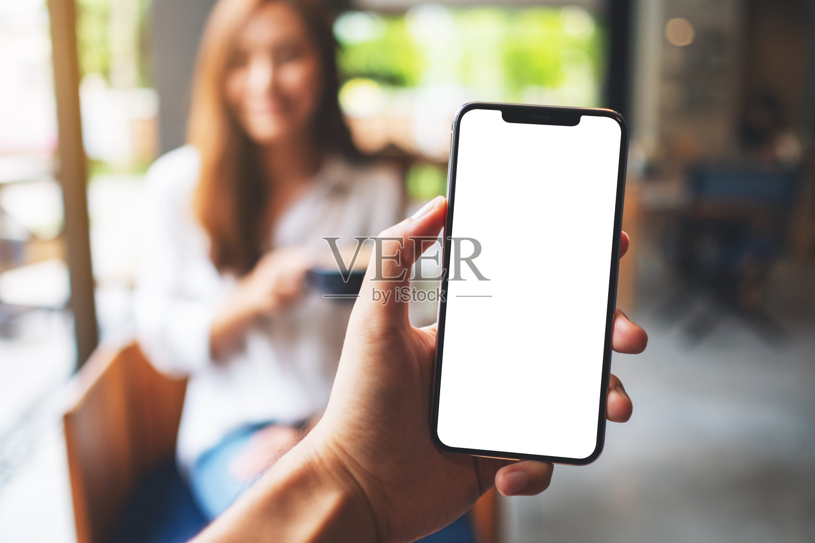 一个男人的手拿着手机的空白屏幕和一个女人在咖啡馆喝咖啡照片摄影图片