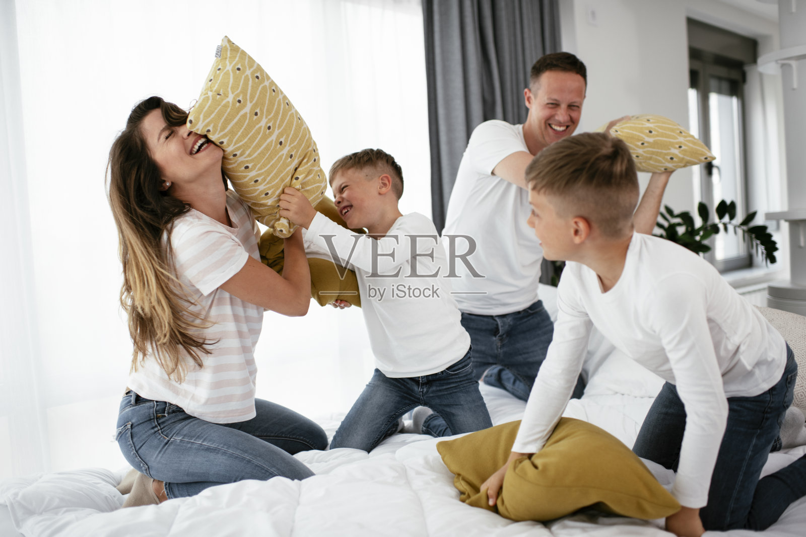 年轻的父母带着儿子在床上争抢枕头。照片摄影图片