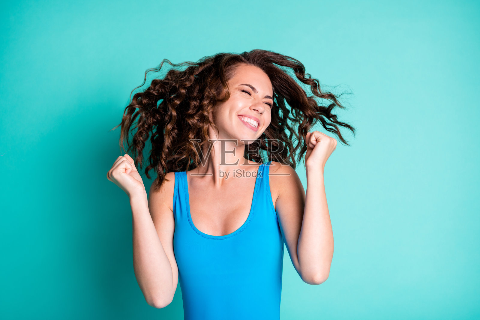 兴高采烈的女孩庆祝泳池派对比赛的照片赢得闭上眼睛举起拳头穿蓝色的紧身衣孤立在蓝绿色的背景照片摄影图片