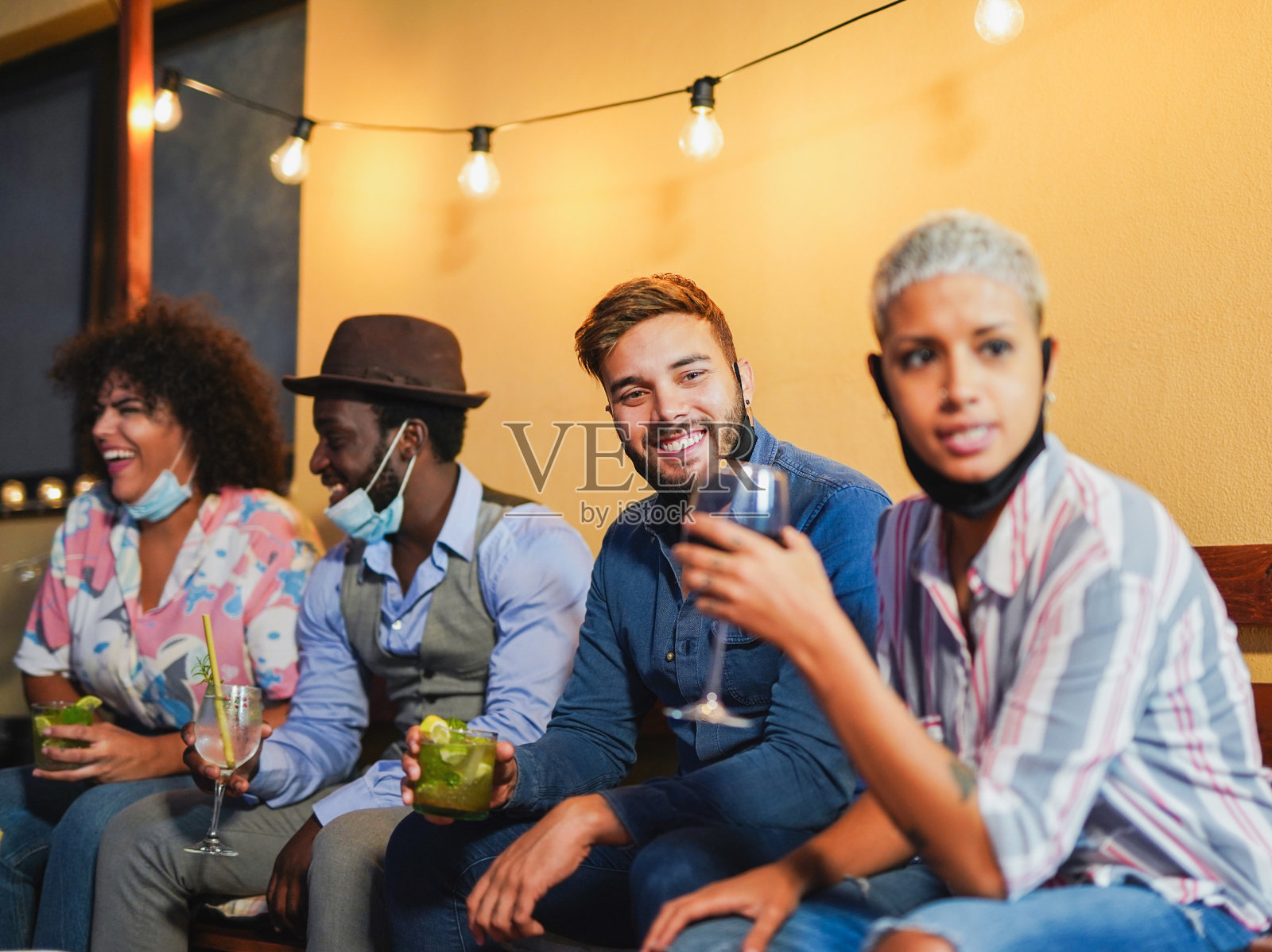 快乐的多种族朋友，手拿鸡尾酒，下巴戴着外科口罩，在家户外庆祝——冠状病毒生活方式照片摄影图片