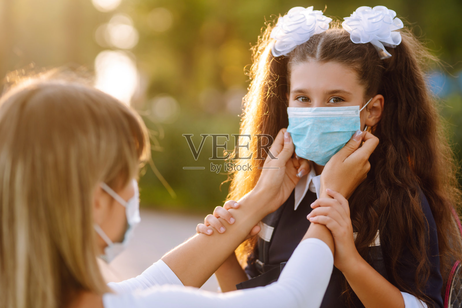 慈爱的母亲帮助戴医用口罩的女学生外出。照片摄影图片