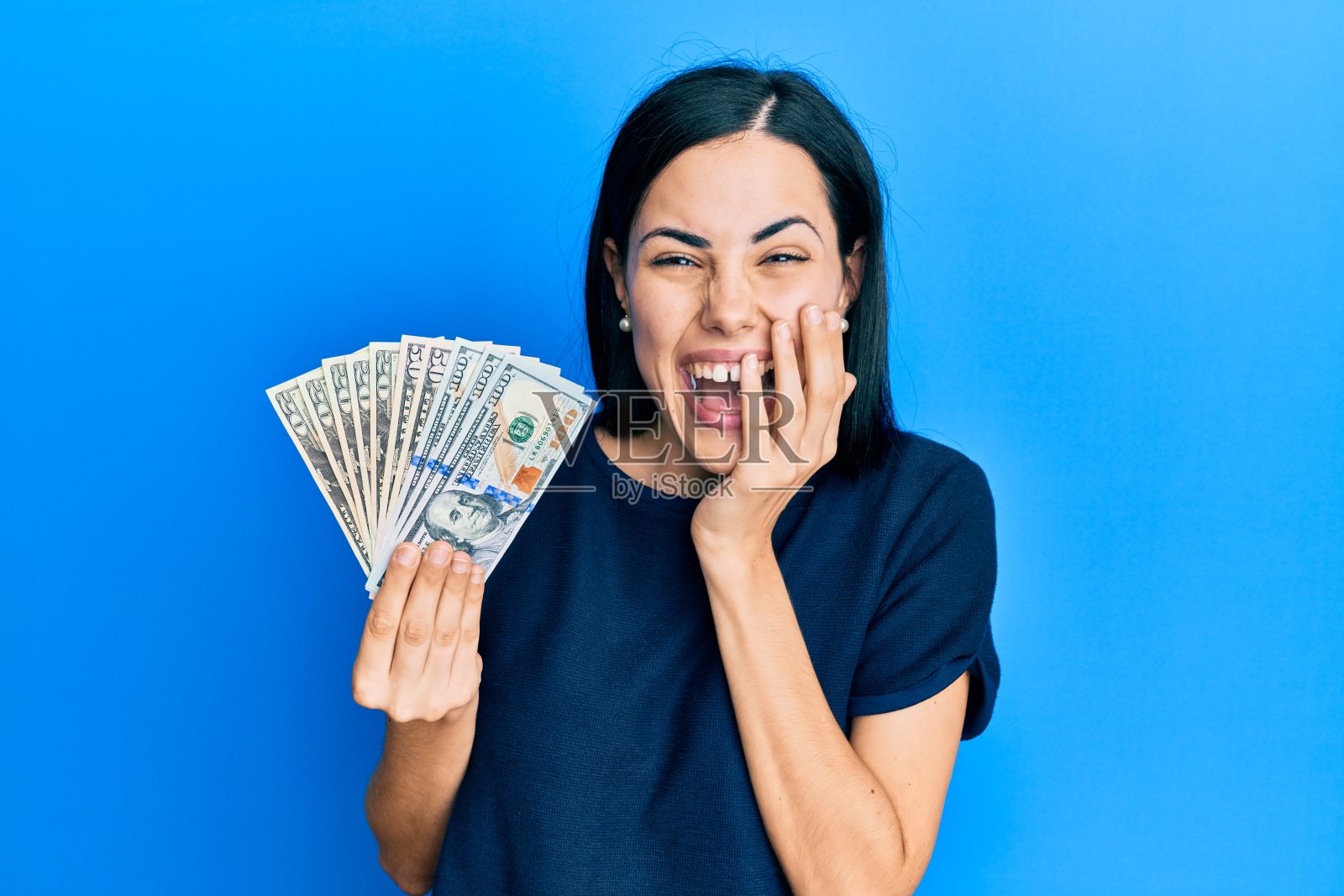 美丽的年轻女子拿着美元大笑，尴尬地傻笑着用手捂着嘴，八卦和丑闻的概念照片摄影图片