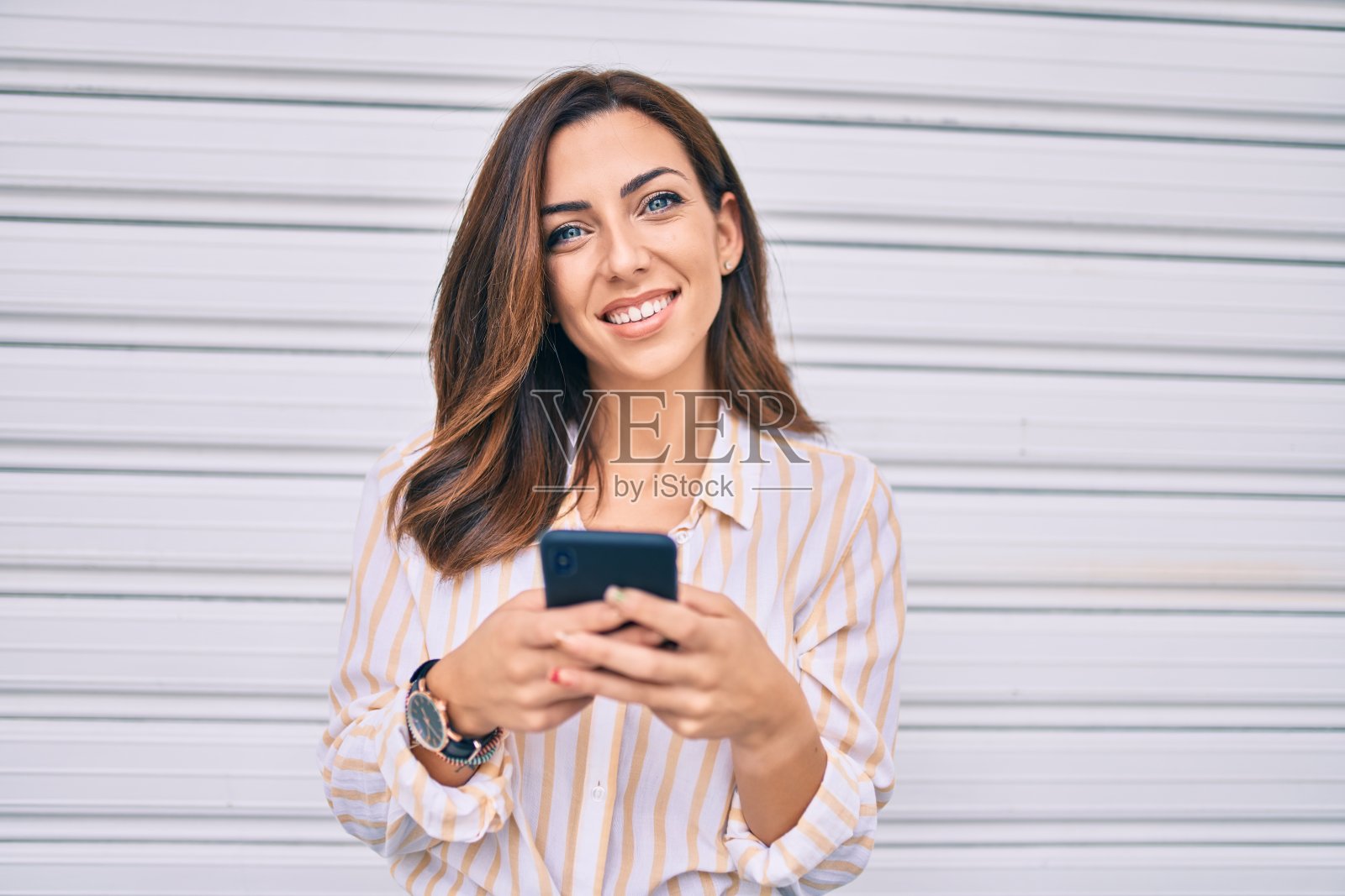 年轻的西班牙裔女性在城市里用智能手机开心地微笑。照片摄影图片