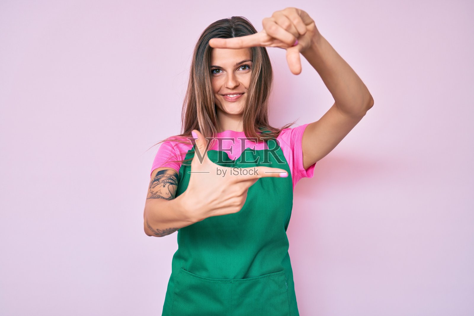 美丽的白人妇女穿着专业围裙微笑做框架与手和手指与幸福的脸。创意和摄影概念。照片摄影图片