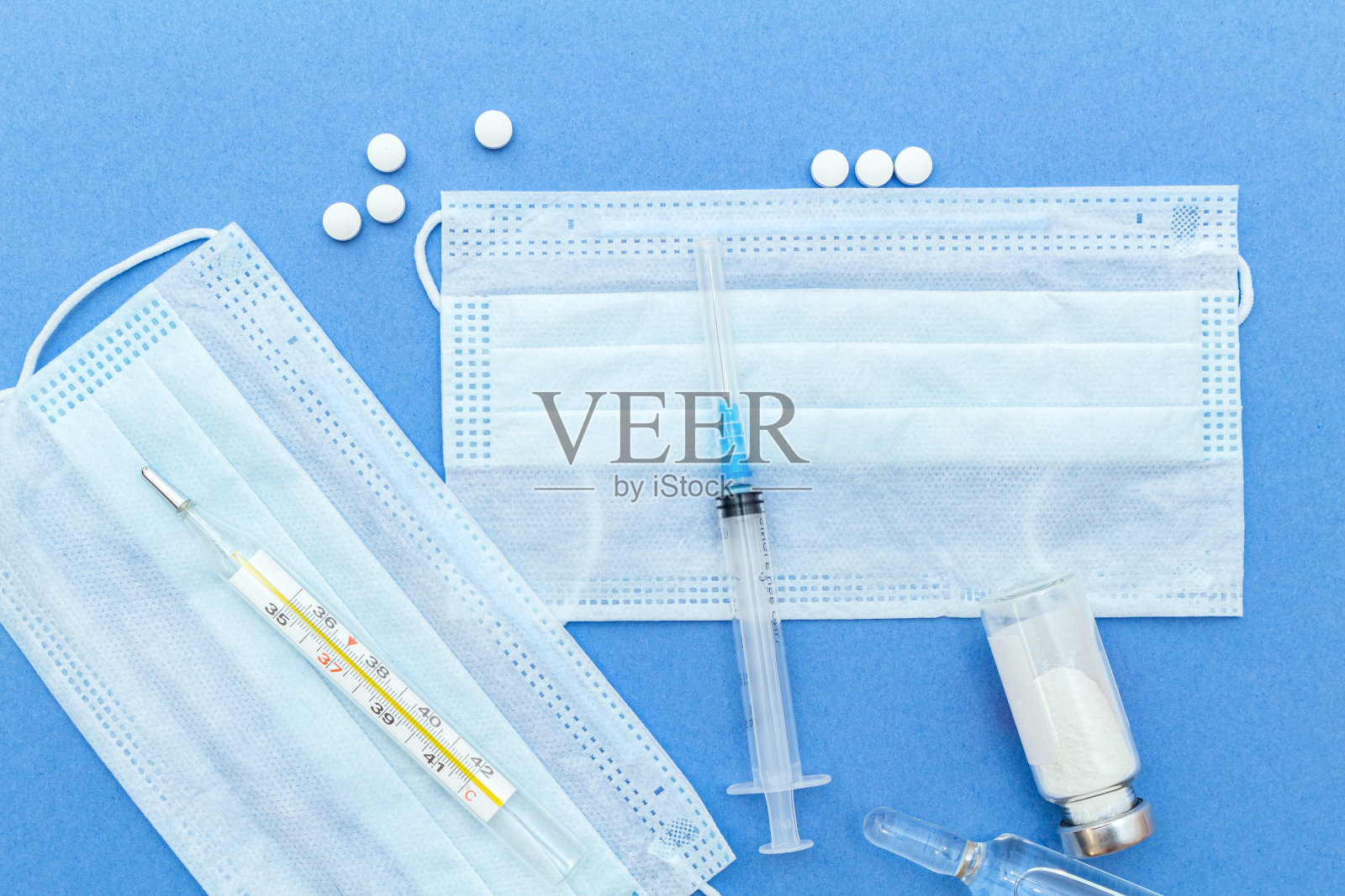 带温度计、注射器、安瓿、药瓶、药片的医用防护口罩，蓝色背景，有拷贝空间。照片摄影图片