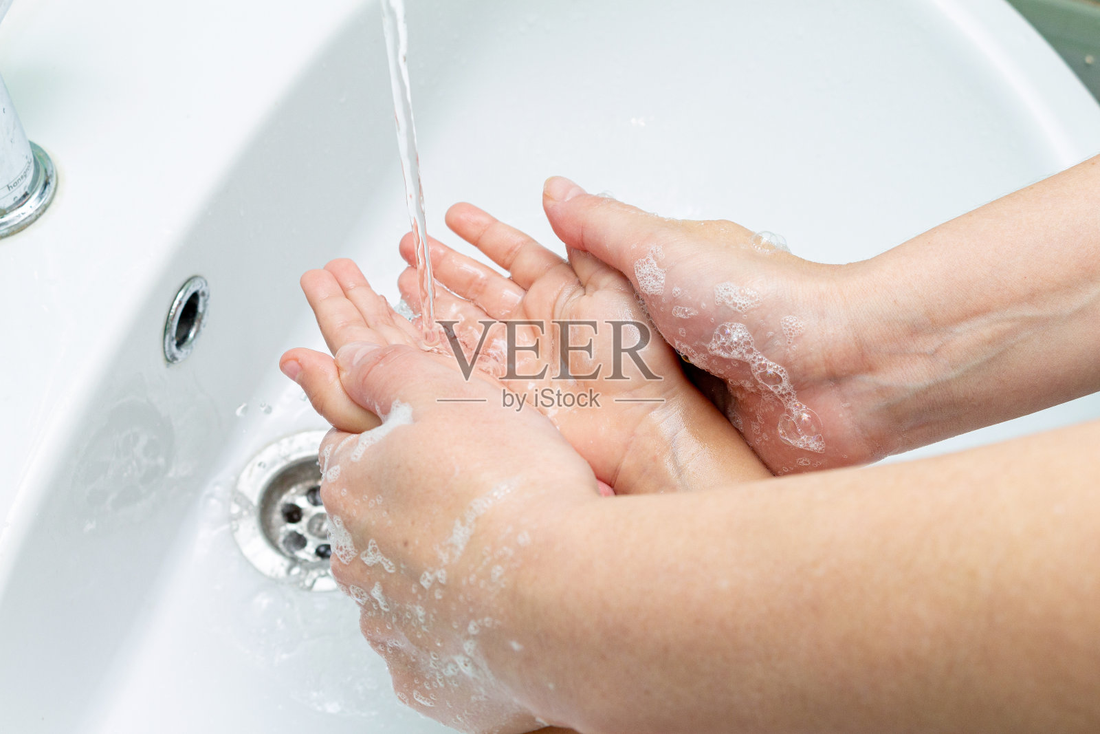 女人在水龙头下帮助孩子洗手照片摄影图片