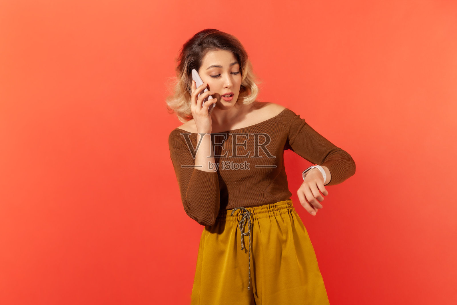 美丽的女人讲电话看手表在她的手腕，约会或约会照片摄影图片