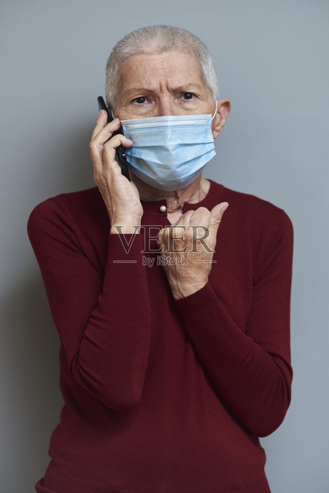 一位戴着面具的老年妇女在她的手机上收到了令人震惊的消息照片摄影图片