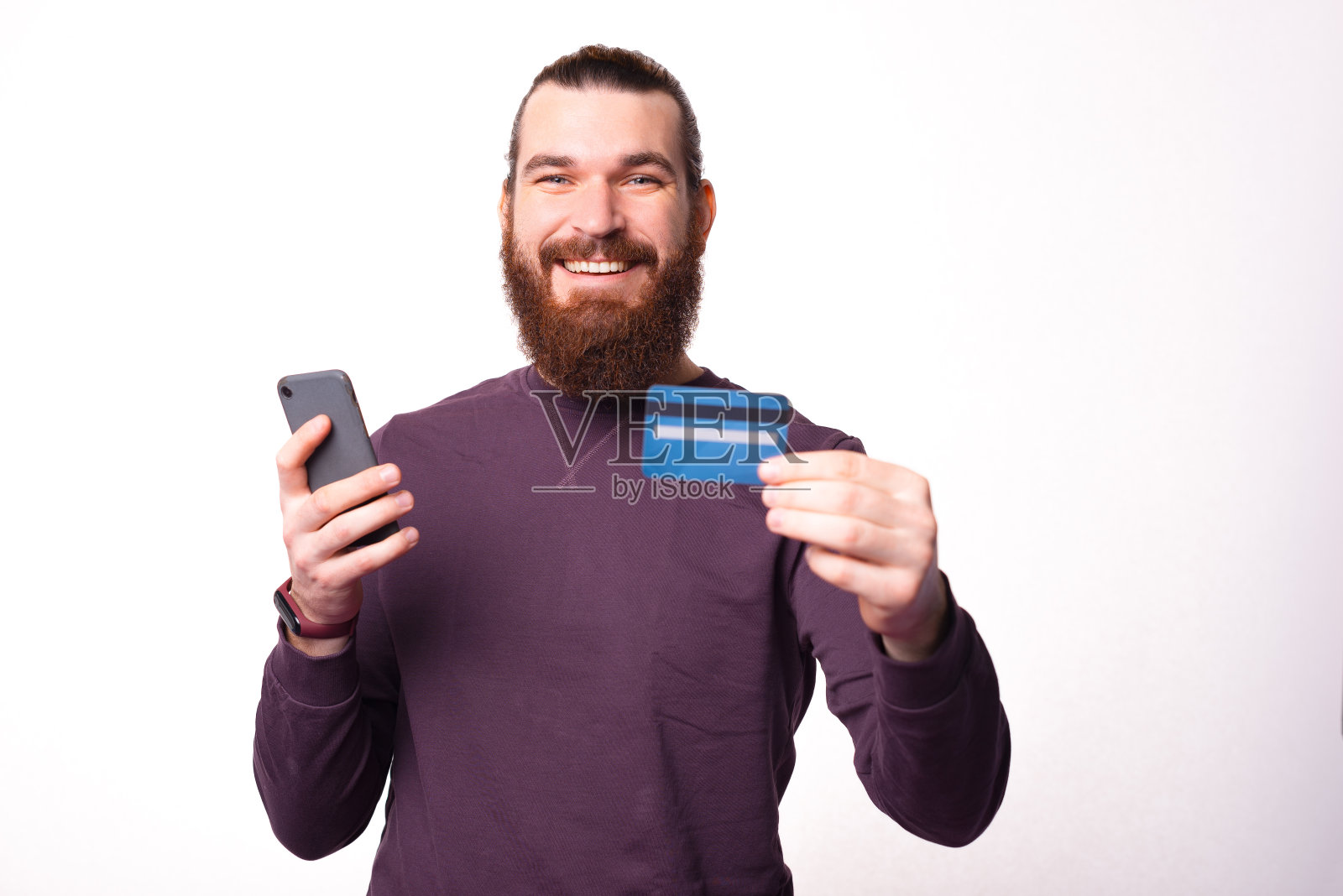 大胡子年轻人拿着信用卡和手机对着镜头微笑照片摄影图片