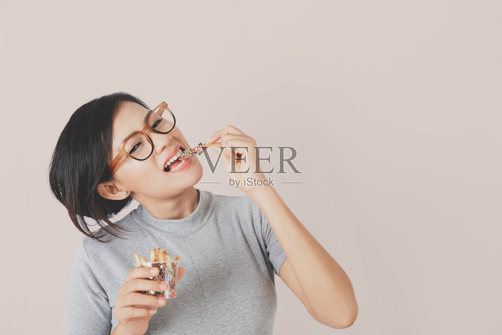 亚洲女人喜欢站在彩色背景上吃零食。专注于脸照片摄影图片