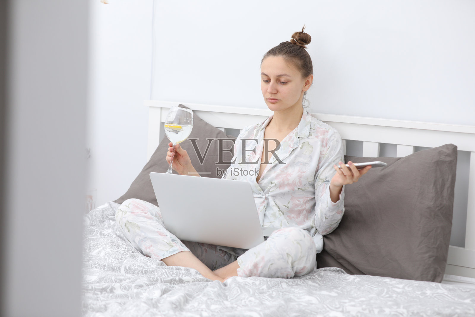 年轻女人在床上放松，边喝葡萄酒边用笔记本电脑。居家、在线学习、远程工作。照片摄影图片