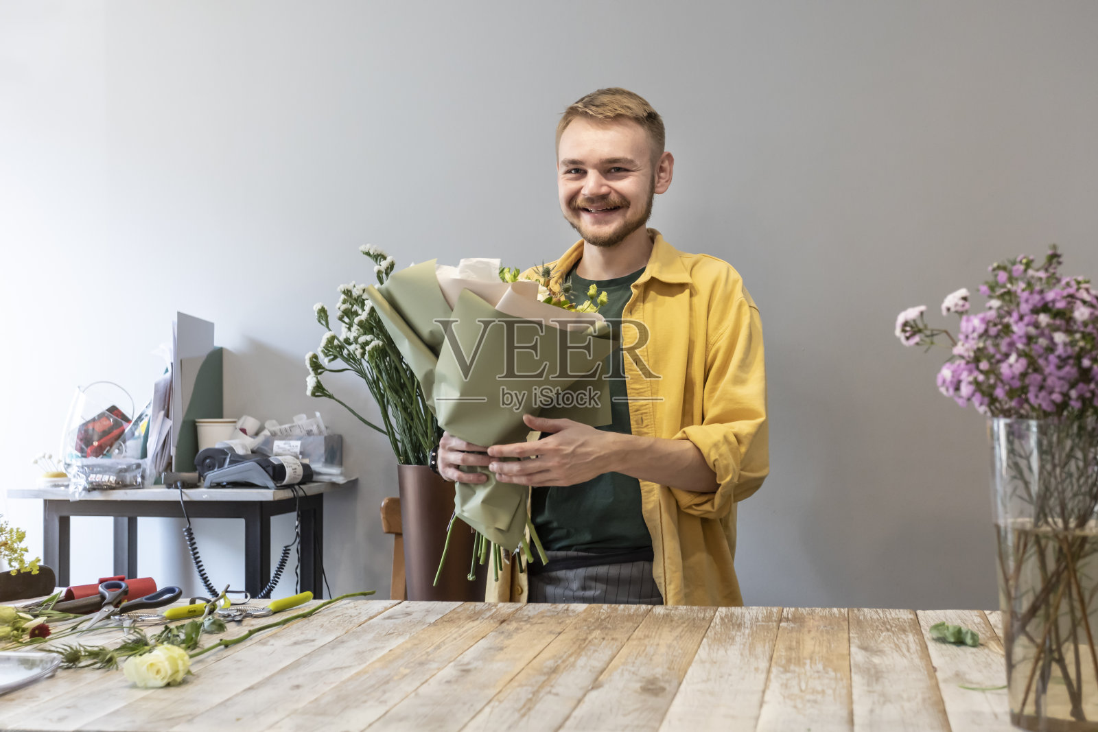快乐的男性花匠拿着一束花在鲜花沙龙会见顾客。照片摄影图片
