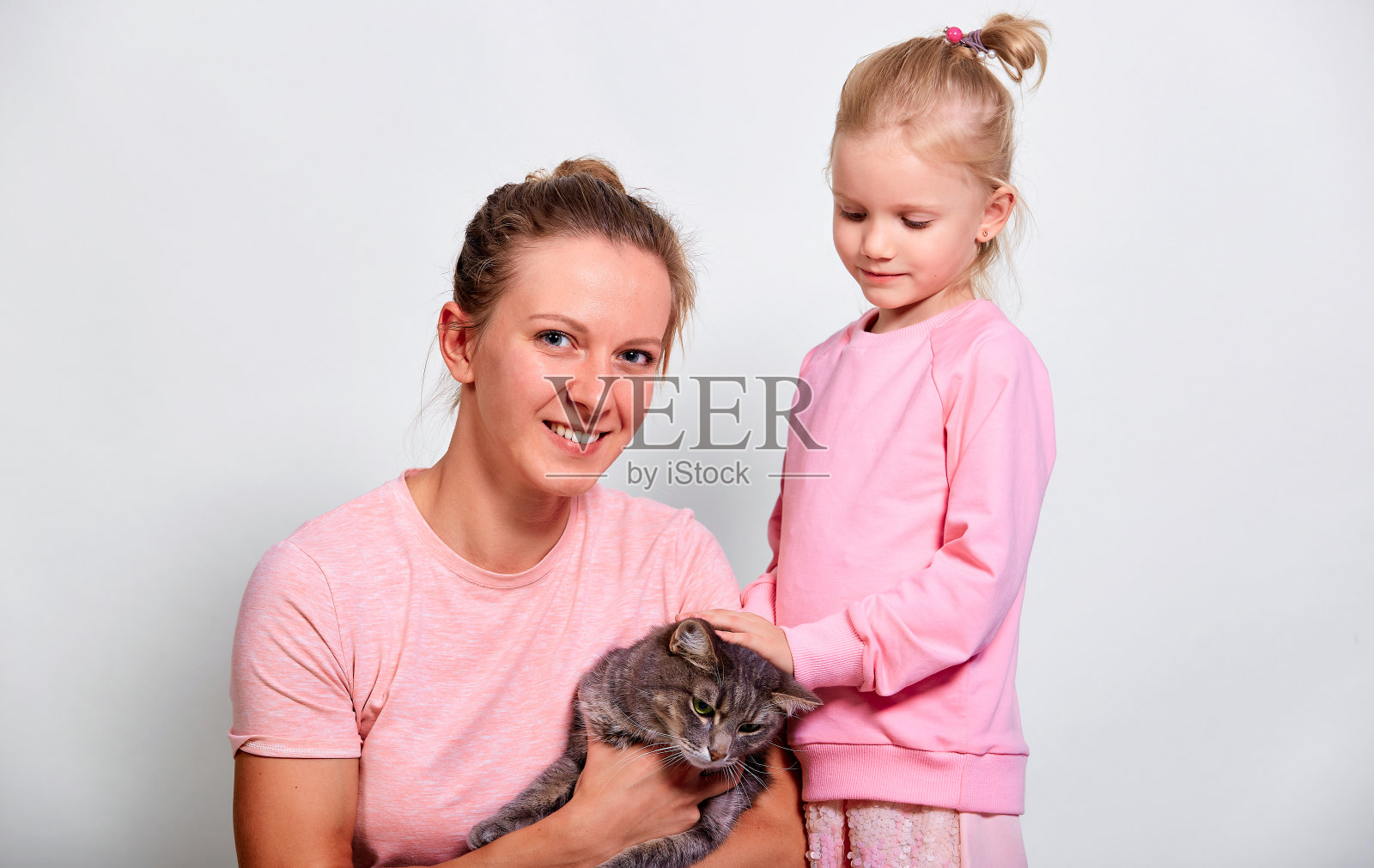 快乐的妈妈和她的女儿抱着猫在灰色的背景照片摄影图片