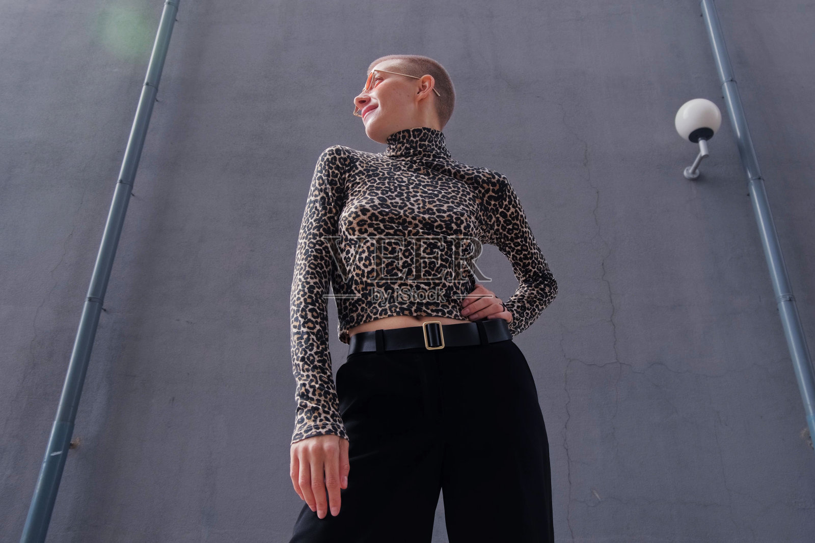 一位穿着豹纹高领毛衣、戴着红色眼镜的短发女子在城市的街道上跳舞、散步、微笑。照片摄影图片