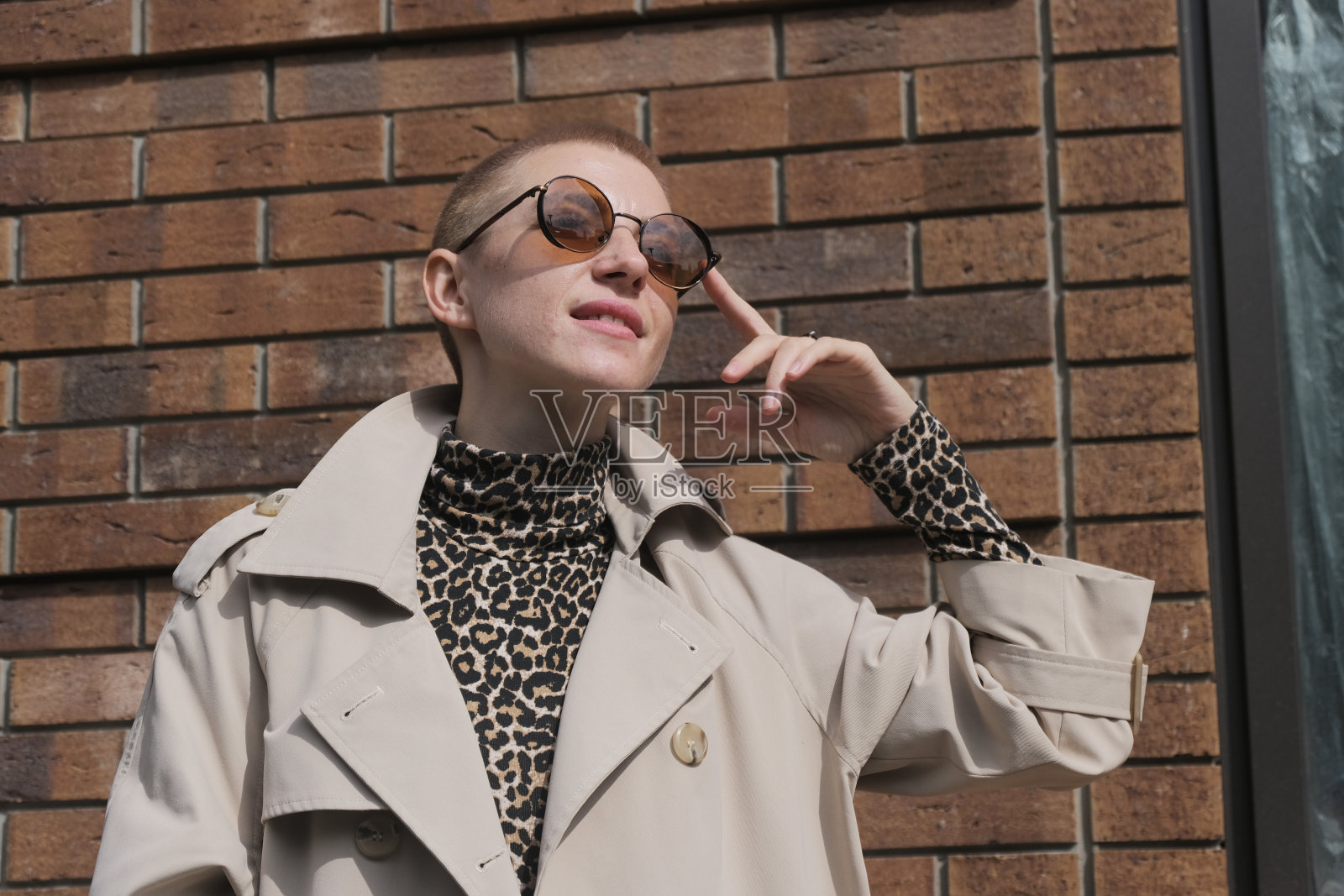 一位穿着豹纹高领毛衣、戴着红色眼镜的短发女子在城市的街道上跳舞、散步、微笑。照片摄影图片