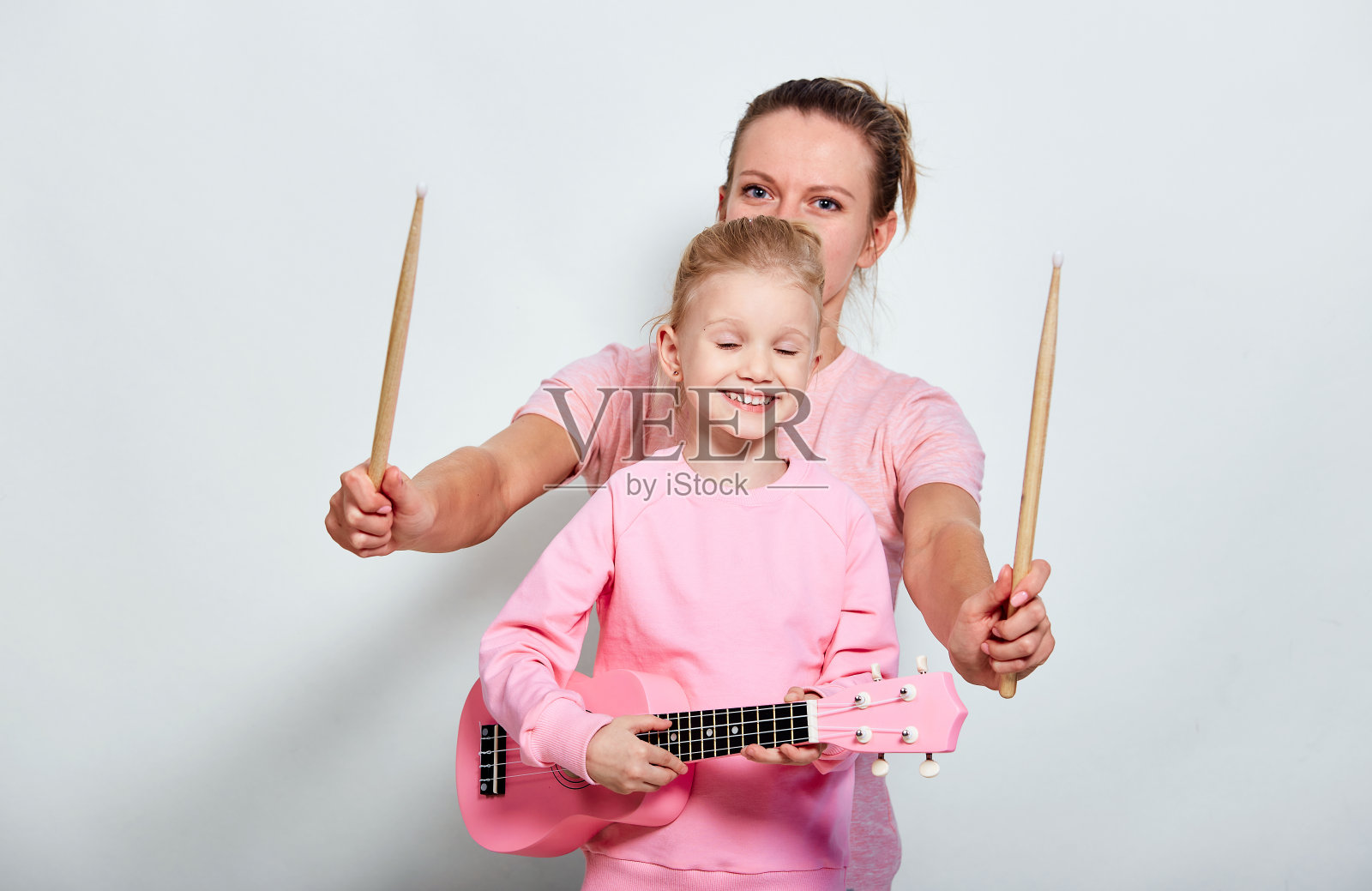 咏母和她漂亮的女儿在弹奏乐器，背景是中性的灰色。一起拿着尤克里里琴和木头鼓槌度过有趣的时光。照片摄影图片