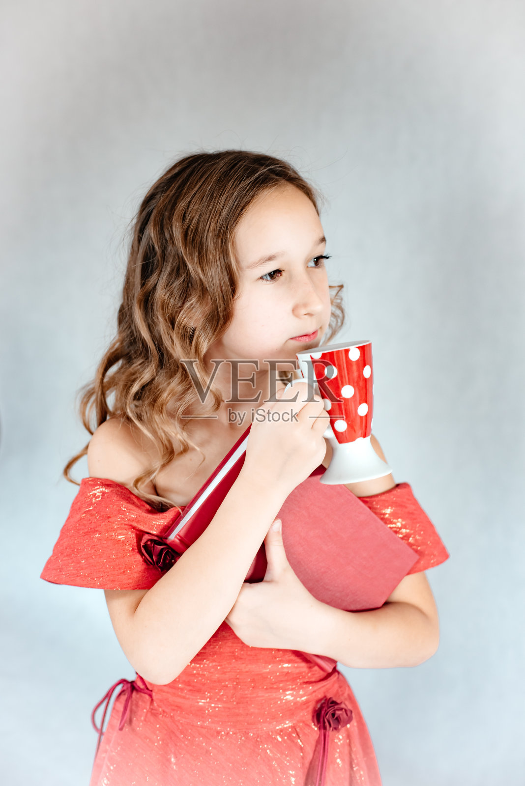 这孩子手里拿着一本书和一个马克杯。照片摄影图片