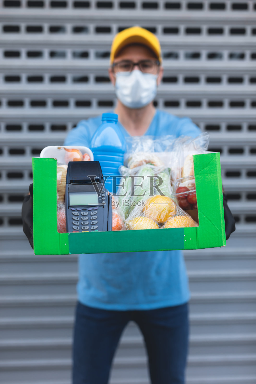 带着保护面罩的快递员，拿着装有杂货和POS机的盒子/袋子，进行非接触式支付。照片摄影图片