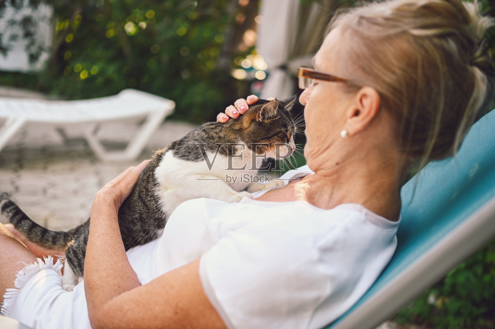 快乐微笑的妇女戴眼镜放松在夏季花园户外拥抱家虎斑猫照片摄影图片