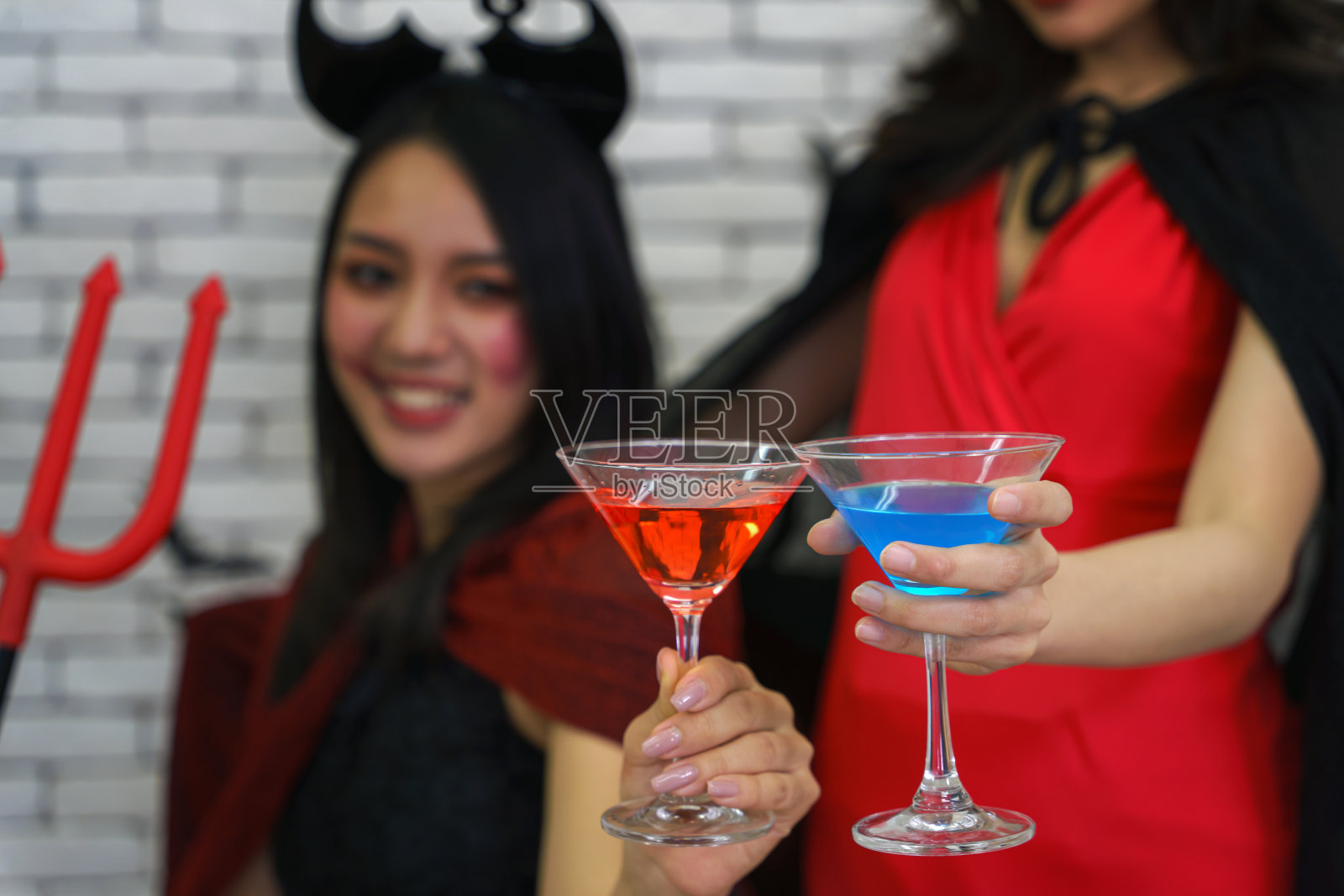 肖像两个亚洲妇女在巫婆的服装拿着鸡尾酒杯万圣节派对照片摄影图片