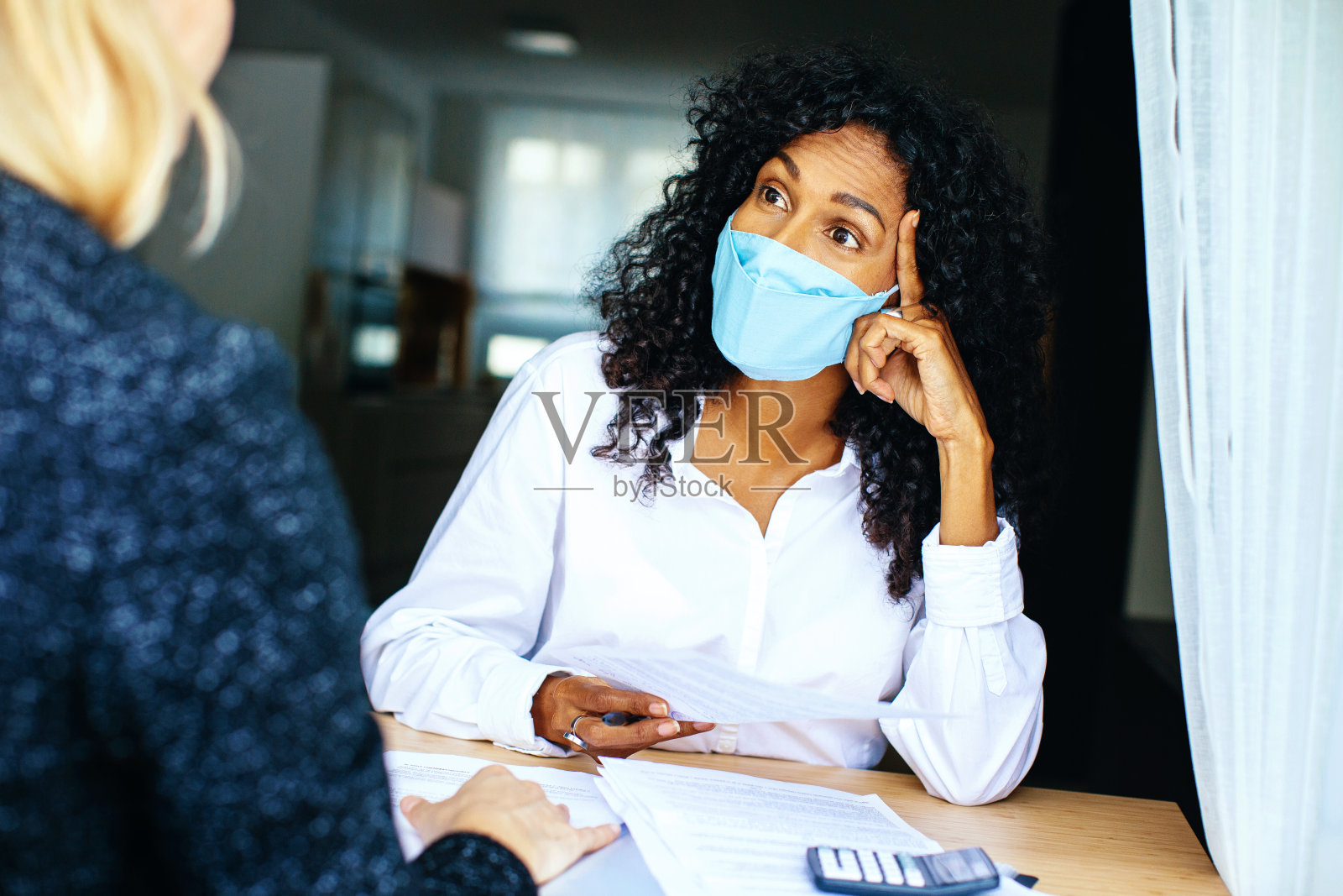 两个人带着面具、合同和计算器坐在办公桌前讨论照片摄影图片