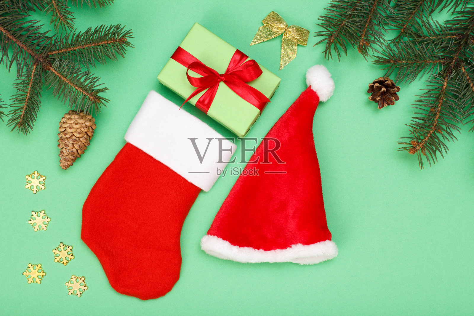 圣诞老人的靴子和帽子，礼物盒，冷杉树枝在绿色的背景照片摄影图片
