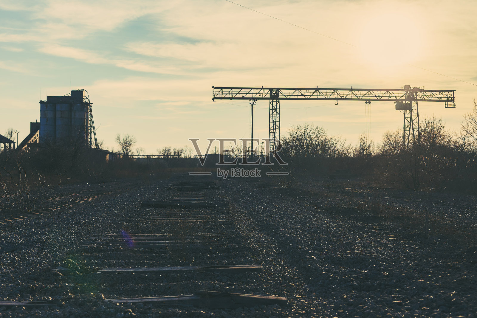 旧的，生锈的门式起重机在铁路上，一个废弃的混凝土工厂。危机、经济崩溃和生产能力的关闭导致了崩溃。全球灾难。一张古老照片的效果。照片摄影图片