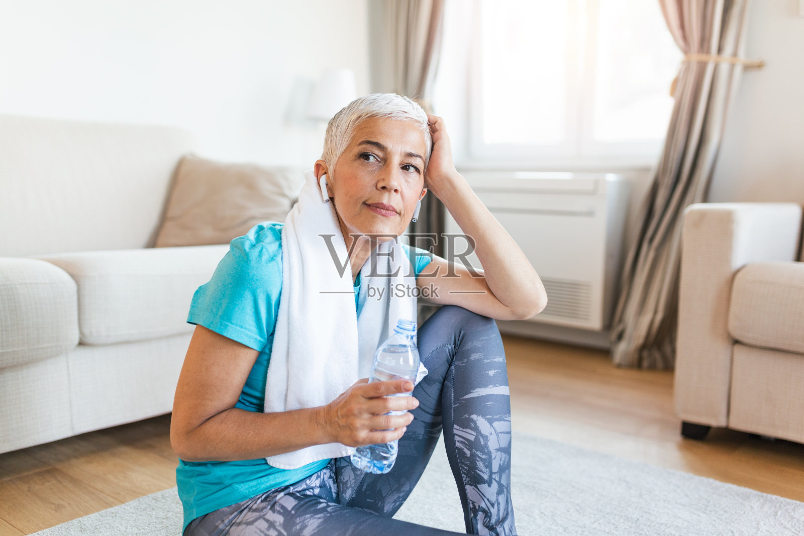 锻炼后戴耳机的老年妇女。拿着一瓶水。成熟的健壮女性在一次良好的锻炼后休息照片摄影图片