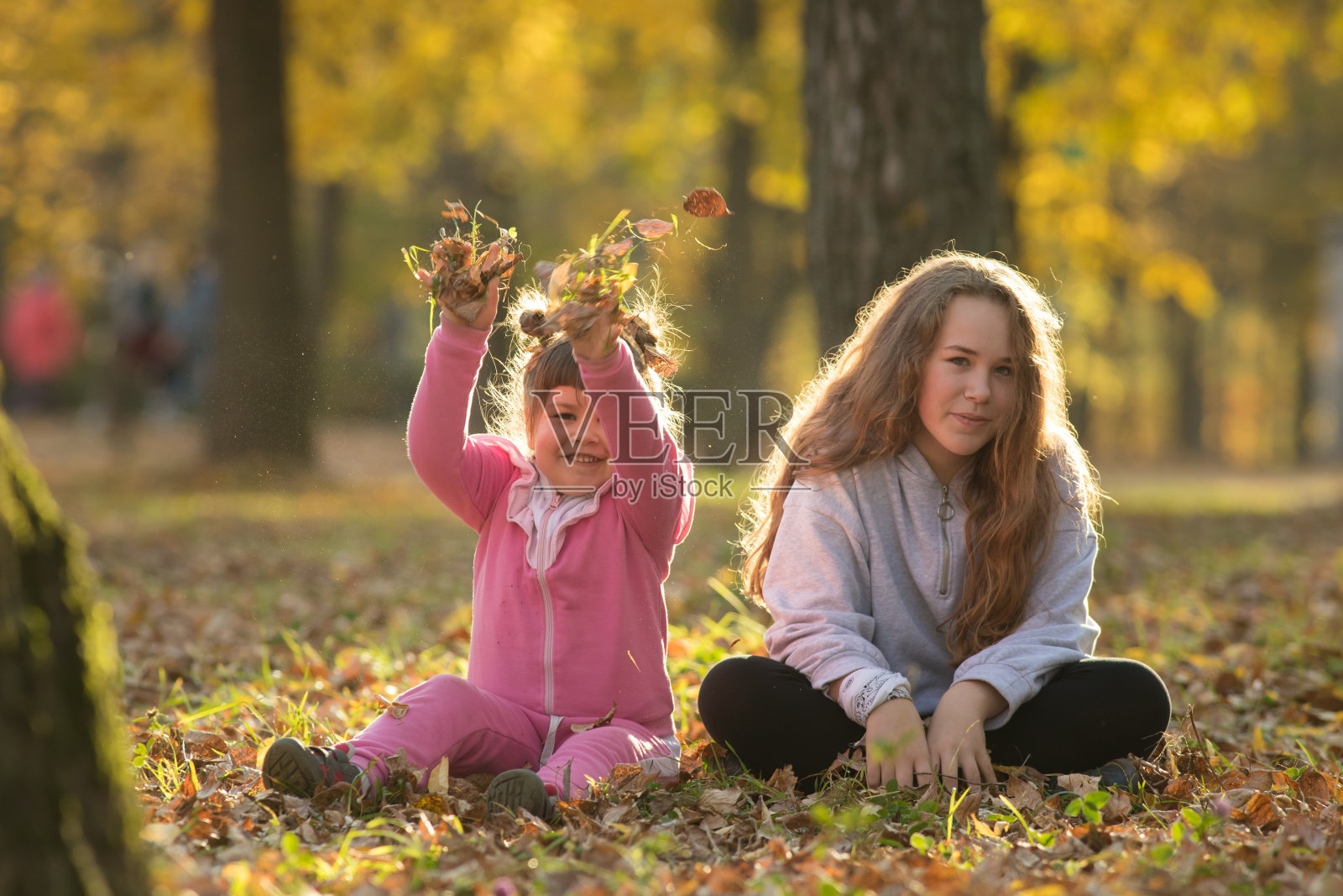 两姐妹坐在秋天公园的地上照片摄影图片