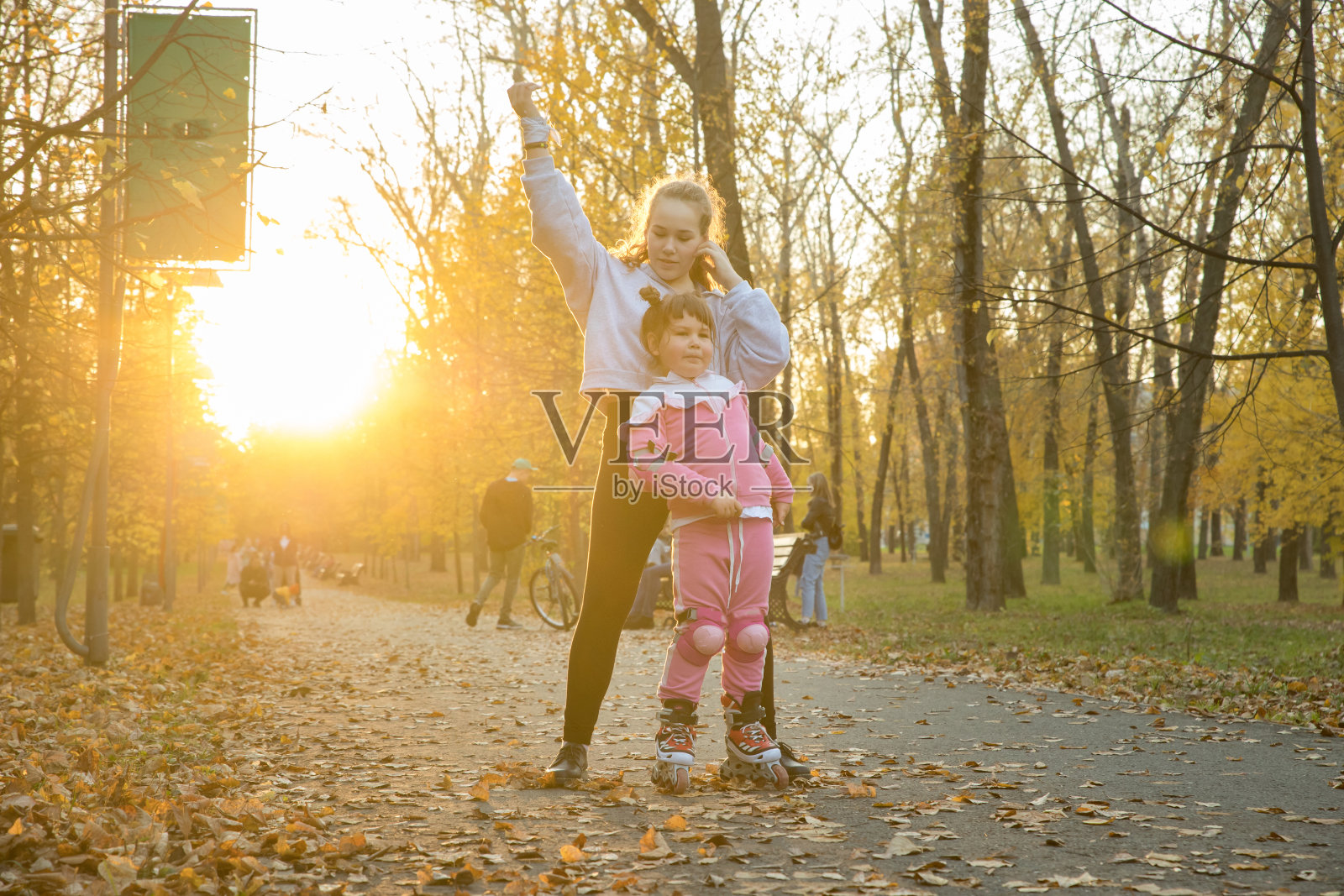 两姐妹在秋天的公园里散步——一个小女孩骑在滚轮上照片摄影图片