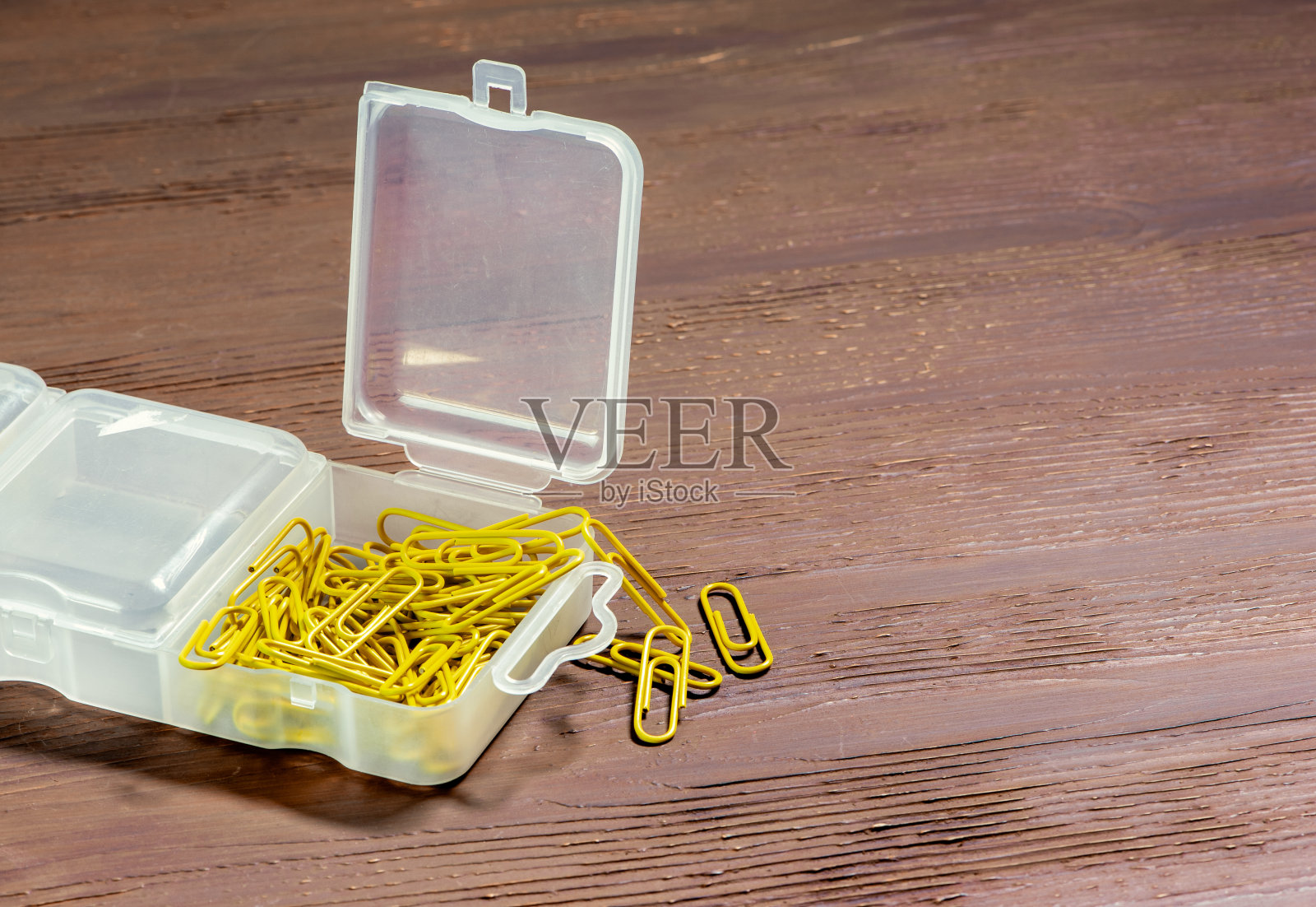 黄色的回形针装在一个塑料盒子里放在一张木头桌子上。为文本复制空间。照片摄影图片