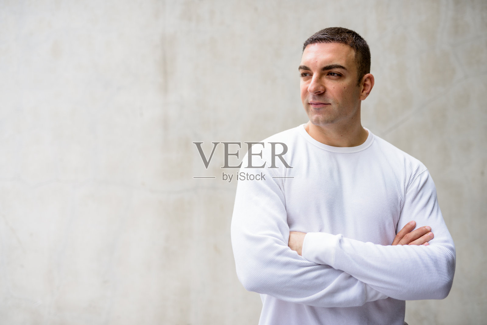 英俊的男人，双臂交叉倚靠在水泥墙上思考照片摄影图片