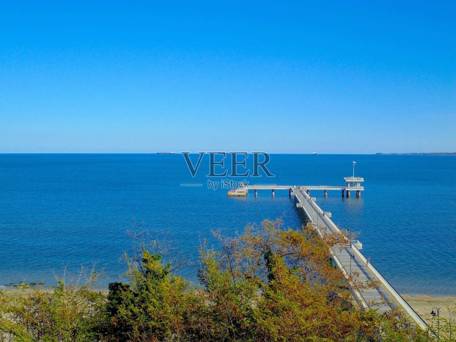 蔚蓝的天空，翠绿的蓝色，透明的海滩，大码头和秋天金色的叶子照片摄影图片