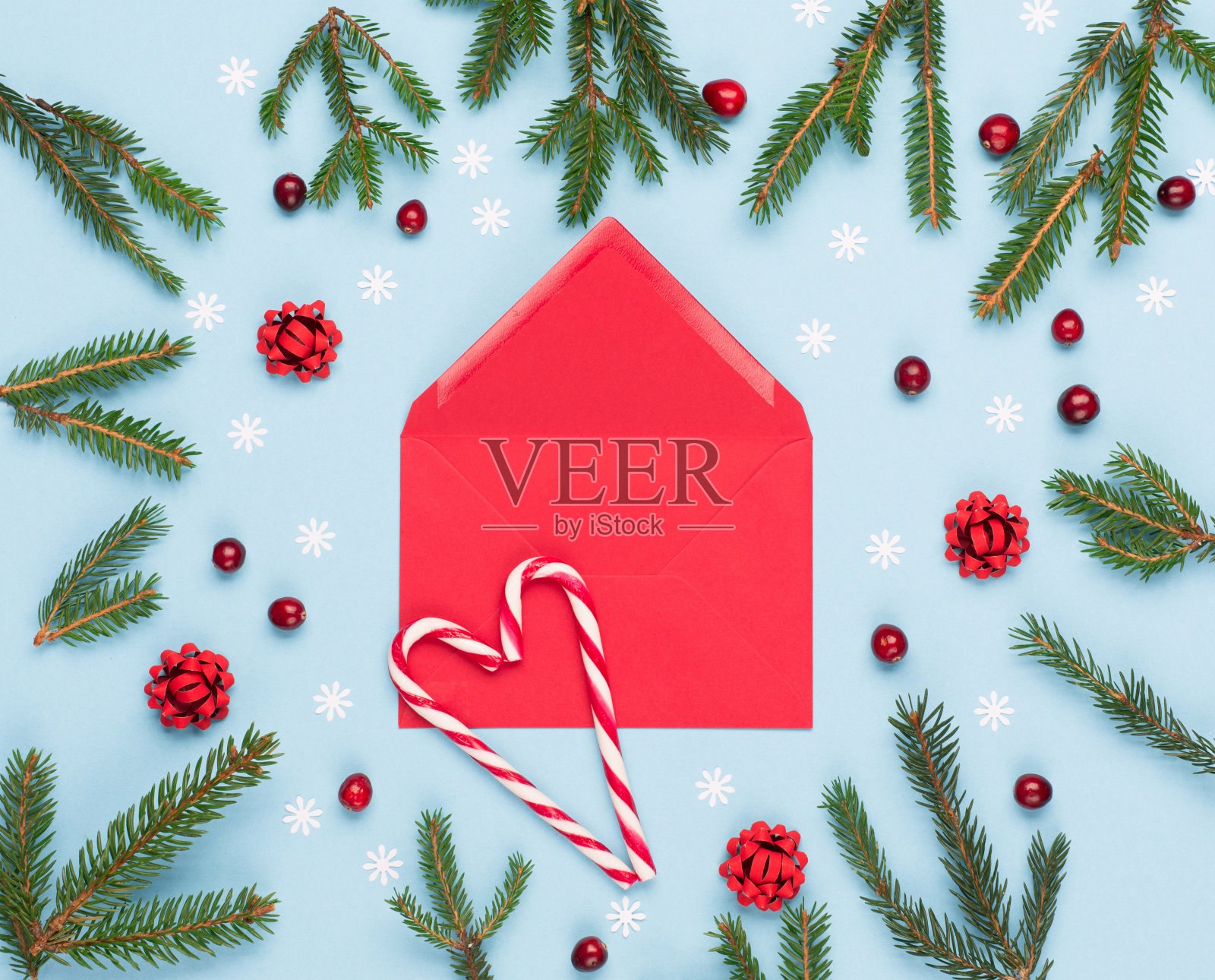 圣诞节的红色空信封，冷杉树枝，红蔓越莓和糖果拐杖在柔和的蓝色背景。照片摄影图片