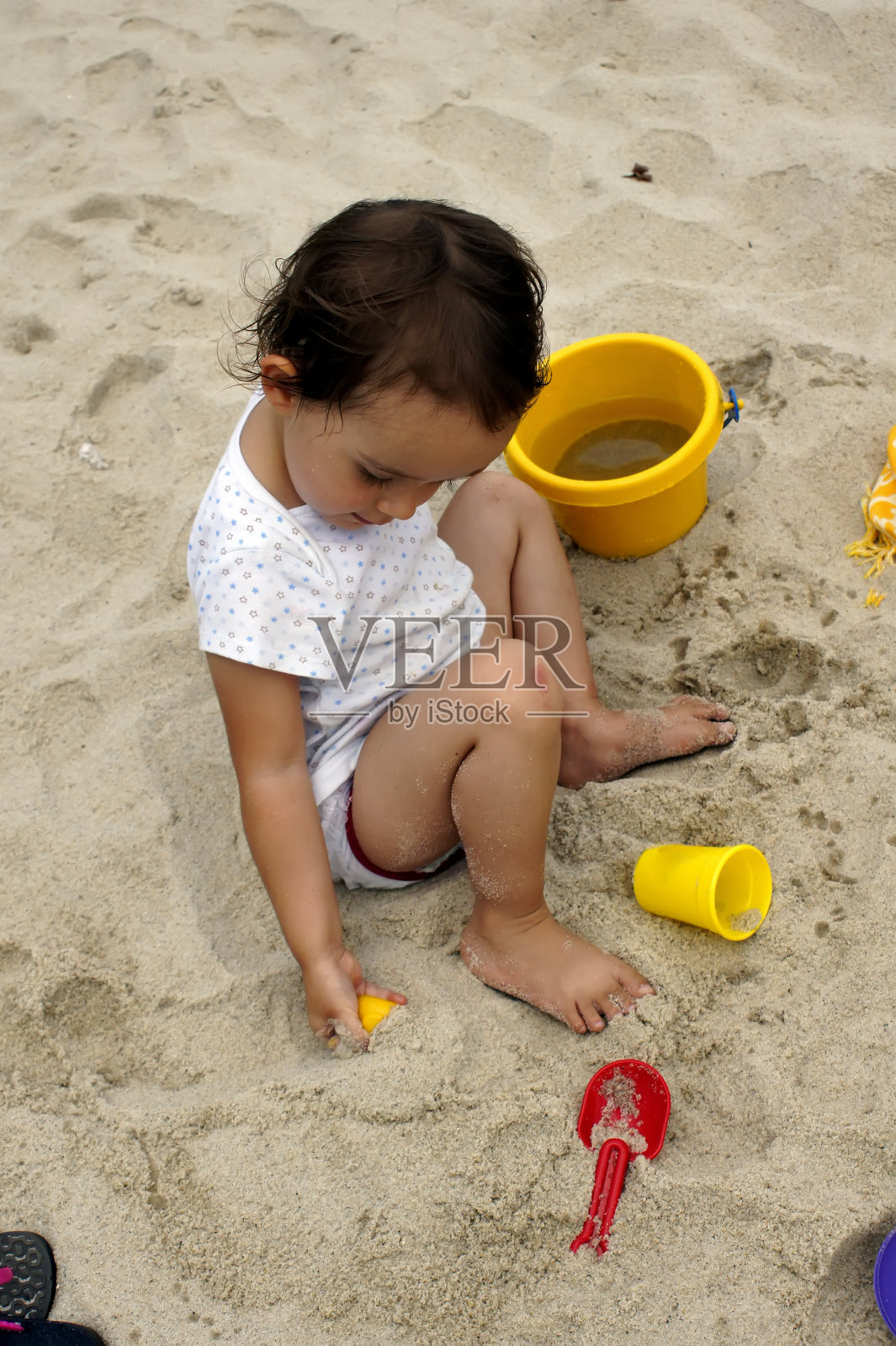 一个在沙滩上玩沙子和水的婴儿。照片摄影图片