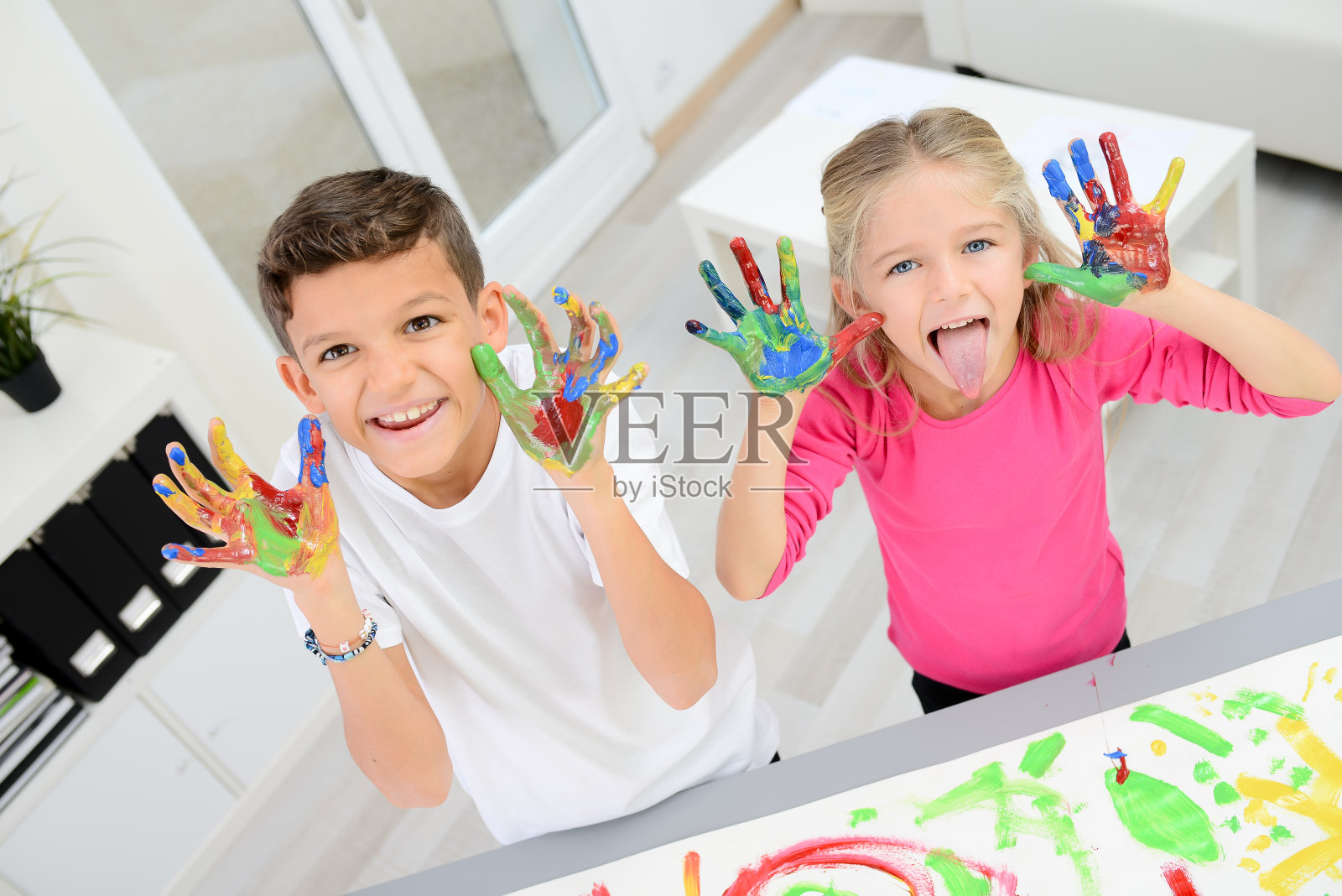 两个漂亮的小男孩和女孩用彩色颜料在白纸上手绘照片摄影图片