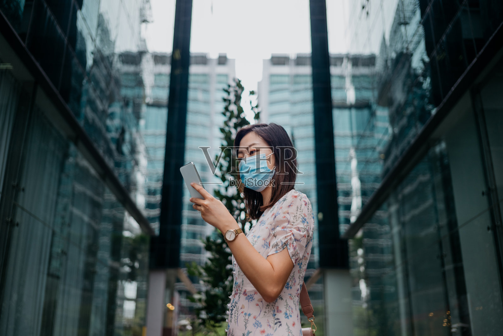 年轻的亚洲女性戴着防护口罩，使用智能手机照片摄影图片