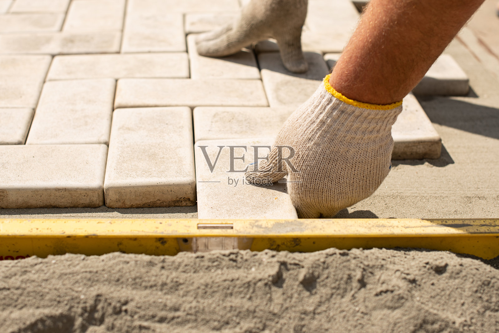 师傅一层一层地铺铺路石。花园砖铺路。在砂土基础上铺设房屋庭院的混凝土铺装板照片摄影图片