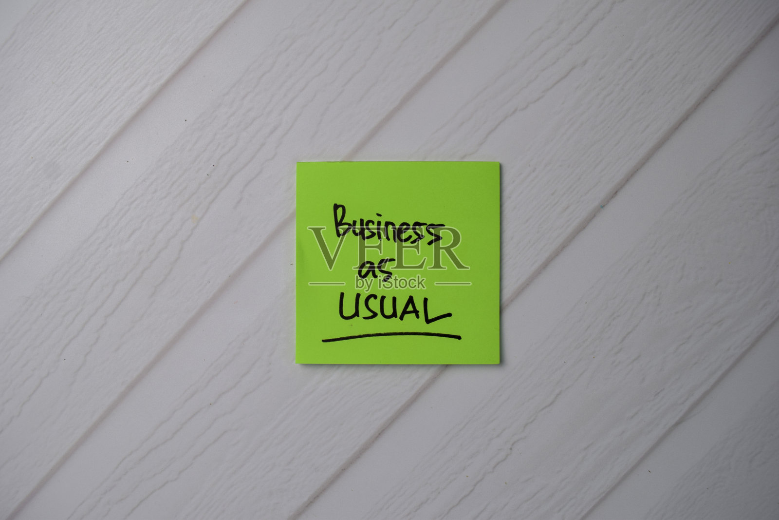 在办公桌边的便利贴上写着“一如既往”。随手贴在办公桌上的便签上。照片摄影图片