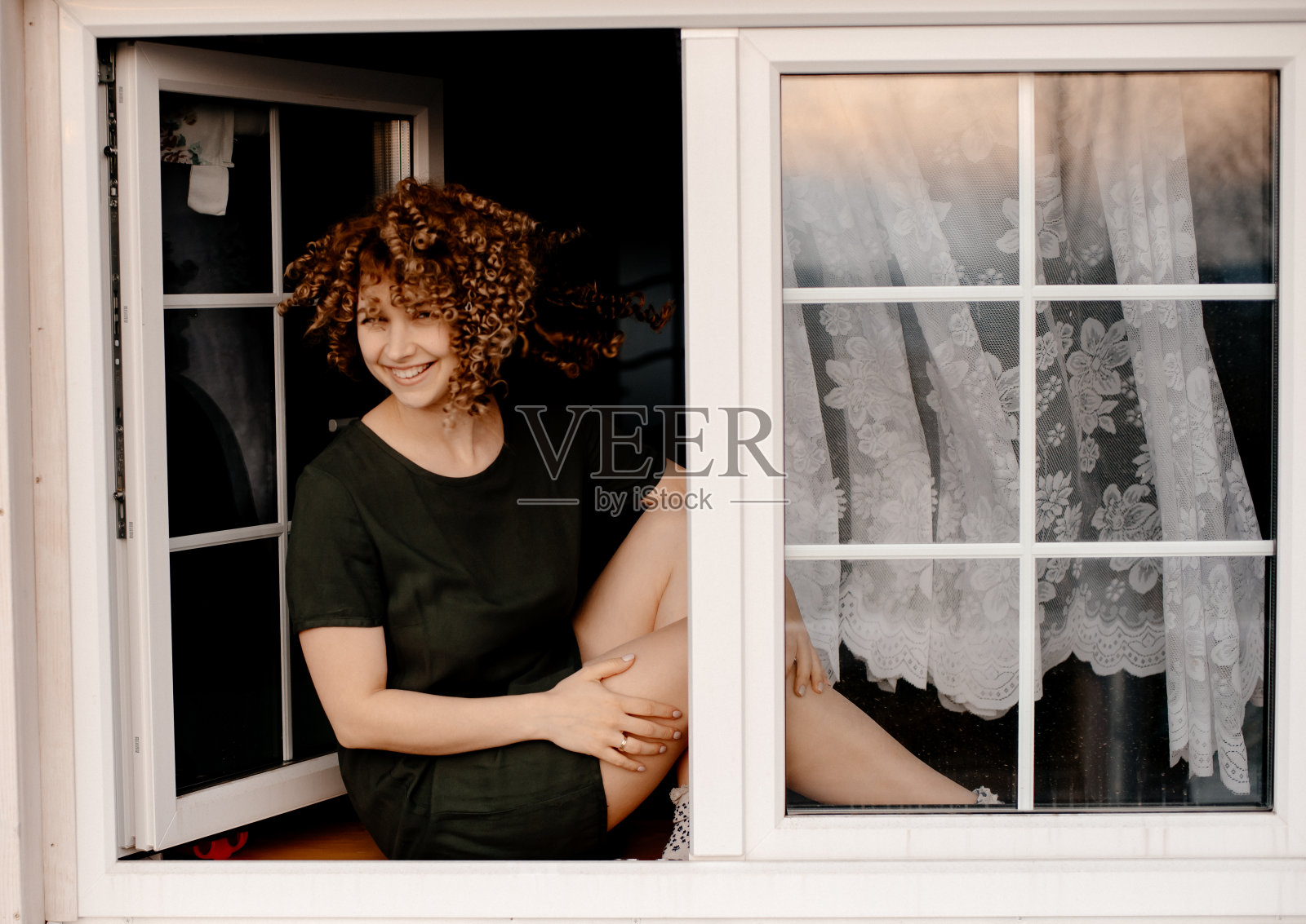 一个漂亮的卷发女孩坐在窗边的窗台上。照片摄影图片