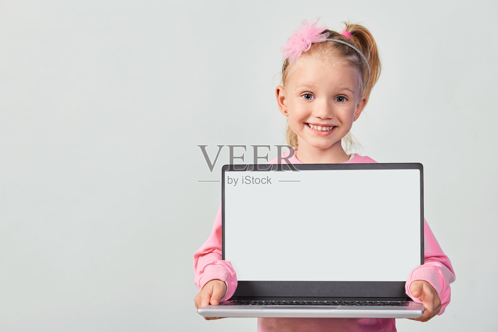 特写肖像Ñute女孩4-5岁在粉红色显示笔记本电脑屏幕与模拟在灰色的背景照片摄影图片